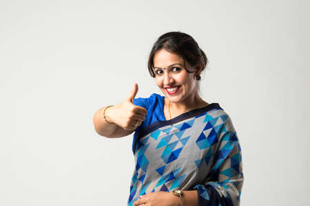 Portrait of successful pretty Indian young woman in sari or saree, with hands folded or thumbs up,...