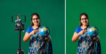 Portrait of Indian lady teacher in saree stands against green, white or blackboard , conducting...