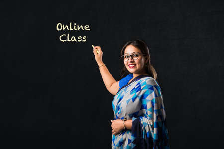 Portrait of Indian lady teacher in saree stands against green, white or blackboard , conducting online class using Camera, internet and lightsの写真素材