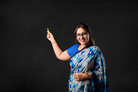 Portrait of Indian lady teacher in saree stands against green, white or blackboard , conducting online class using Camera, internet and lightsの写真素材