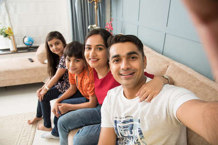 Indian family sitting on sofa and taking selfie picture using smartphoneの写真素材