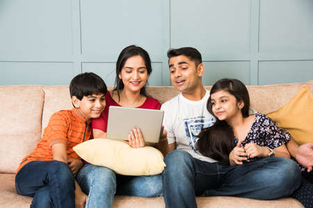Indian family sitting on sofa and using smartphone, laptop or tablet, watching movie or surfing internetの写真素材
