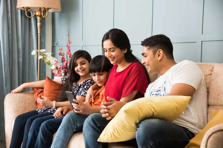 Indian family sitting on sofa and using smartphone, laptop or tablet, watching movie or surfing internetの写真素材