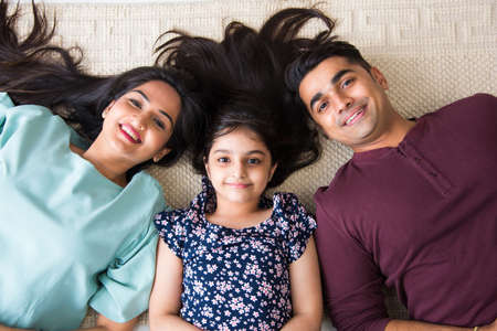 Portrait of happy Indian Asian young family while sitting on sofa, lying on floor or sitting against wallの写真素材