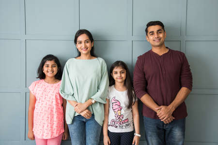 Portrait of happy Indian Asian young family while standing against wall, parents with two daughters looking at cameraの写真素材