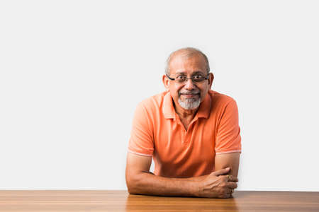 Portrait of Indian asian senior man sitting at table presenting or in success pose