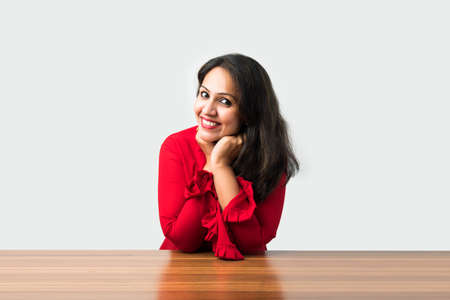 Indian asian pretty woman standing at table resting chin on handsの写真素材