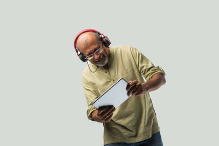happy senior Indian asian bearded man smiling using headphones with smartphone or tablet against...