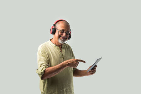 happy senior Indian asian bearded man smiling using headphones with smartphone or tablet against...