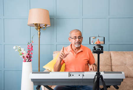 Senior Asian Indian musician performing while taking online music class or recording video on...