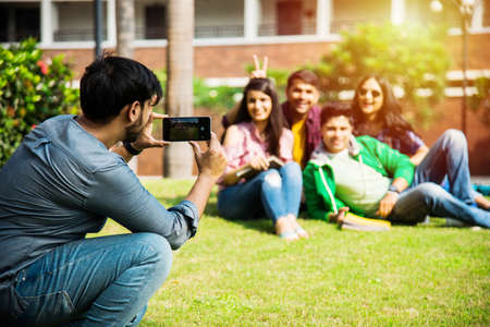 Asian Indian college students taking selfie picture using smartphone in campus while sitting on stairs or lawn, having funの写真素材