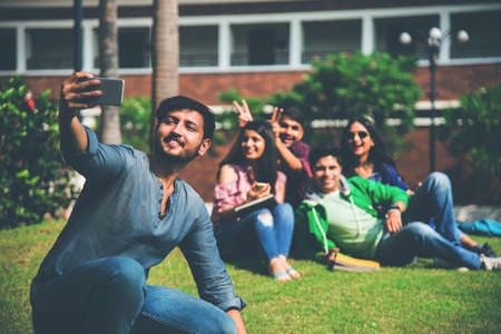 Asian Indian college students taking selfie picture using smartphone in campus while sitting on...
