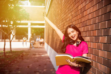 Asian Indian college student in focus working on laptop or reading book while other classmates in the background, outdoor picture in university campusの写真素材