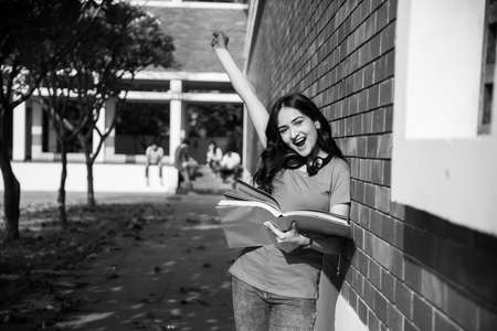 Asian Indian college student in focus working on laptop or reading book while other classmates in the background, outdoor picture in university campusの写真素材