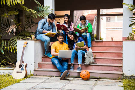 Young Asian Indian college students reading books, studying on laptop, preparing for exam or working...