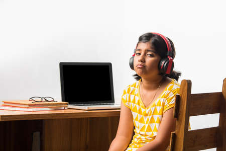 Cute Little Indian girl studying online using her laptop or Tablet computer at home or attending...