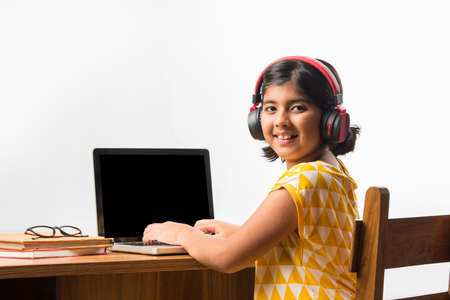 Cute Little Indian girl studying online using her laptop or Tablet computer at home or attending school during corona pandemic or lockdownの写真素材