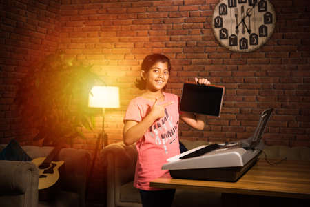 Asian Indian child learning music or musical instrument online using laptop computer or tablet at...