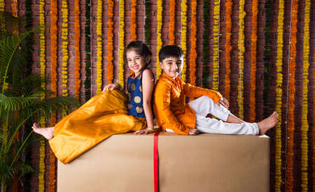 Indian kids, little brother and sister celebrating Diwali, Raksha Bandhan, Bhai Dooj with big gift box and sweet laddooの写真素材