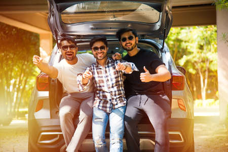 Group of Indian Asian young and attractive friends sitting in the open trunk of a car, a summer road tripの写真素材
