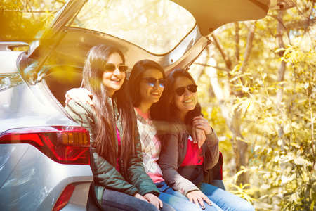 Group of Indian Asian young and attractive friends sitting in the open trunk of a car, a summer road...