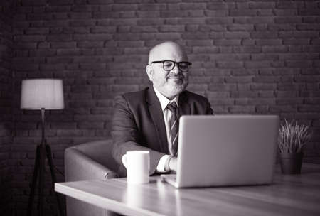 Asian Indian senior financial businessman sitting at his workstation or desk in front of a computer,...