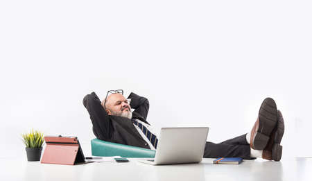 Portrait of a satisfied senior Indian Asian businessman sitting at workplace in front of the...