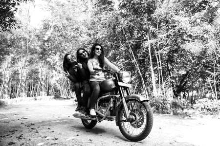 Happy Indian asian happy young woman or female friends riding on motorcycle or motorbike on the forest roadの写真素材