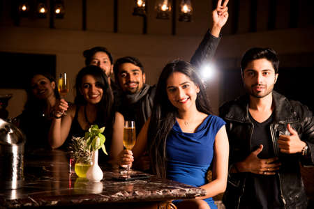 Group of indian asian friends sitting at lounge bar, having drinks or cocktails, celebrating new...