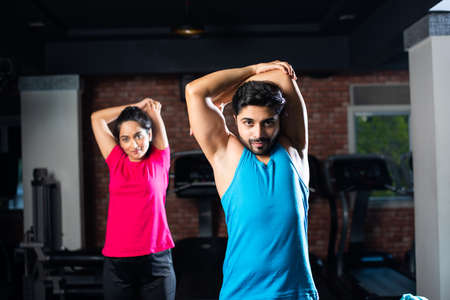 sporty Indian asian young couple stretching in gym post exercise for cooling down, improving...