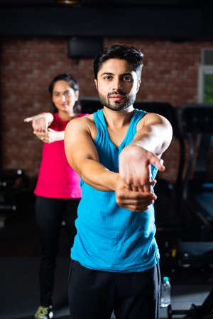 sporty Indian asian young couple stretching in gym post exercise for cooling down, improving flexibilityの写真素材