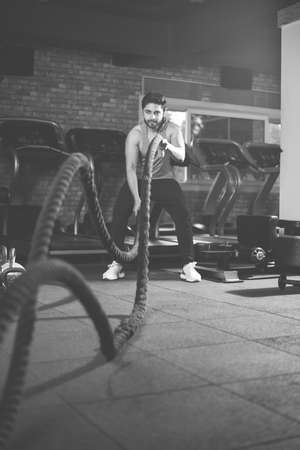 Handsome Indian asian young man doing battle rope exercise while working out in gym, selective focusの写真素材