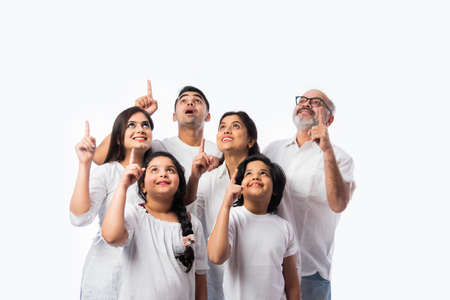 Indian multigenerational family pointing or presenting empty space, standing isolated against white...