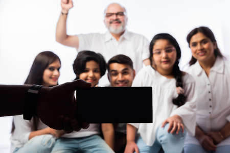 Indian family of six video calling on smartphone or taking selfie picture against whiteの写真素材