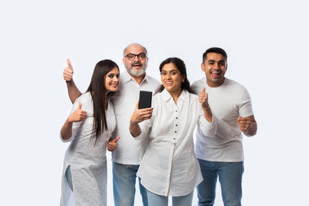 Indian young couple with parents using or holding smartphone with happy expressions, standing...