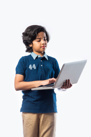 Asian Indian school kid holding and using laptop while standing against white backgroundの写真素材