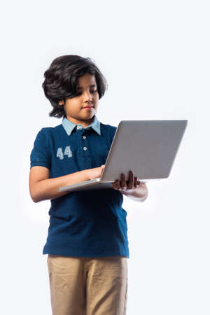 Asian Indian school kid holding and using laptop while standing against white backgroundの写真素材