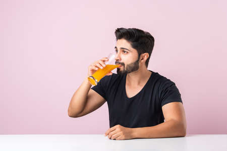 Portrait of a handsome Indian young man drinking orange juice in kitchen in the morningの写真素材
