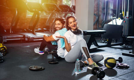 Indian young couple in gym resting or taking break from exercise, drinking water, showing positive...