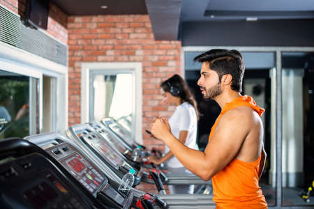 Indian asian attractive couple doing cardio training program in fitness center or gym, selective...