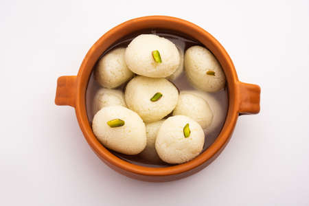 Rasgulla or rosogulla - an Indian sweet made from khoya, soft and spongy, in earthen bowl over yellow napkin and brown backgroundの写真素材
