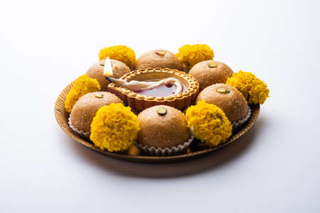 Besan ladoo and diwali diya or clay lamp decorated in a plate with marigold flowers - Happy Diwali...