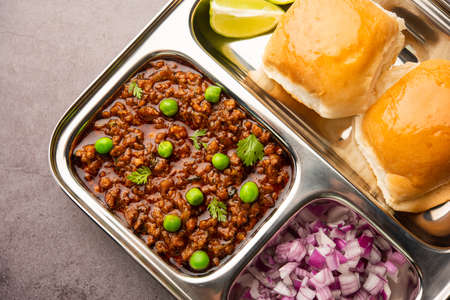 Mutton Kheema Pav OR Indian Spicy Minced Meat served with bread OR kulcha, garnished with green peas. Moody background. Selective focusの写真素材