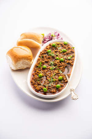 Mutton Kheema Pav OR Indian Spicy Minced Meat served with bread OR kulcha, garnished with green peas. Moody background. Selective focusの写真素材