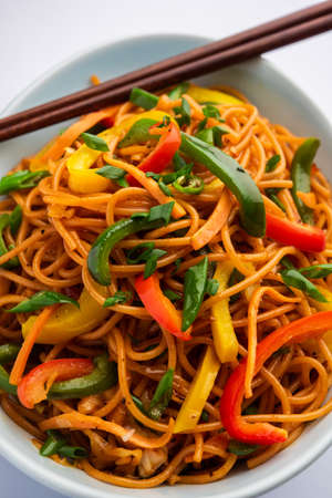 Schezwan Noodles or Szechwan vegetable Hakka Noodles or chow mein is a popular Indo-Chinese recipes, served in a bowl or plate with wooden chopsticksの写真素材