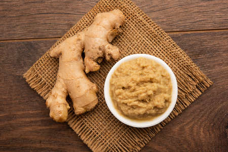 Fresh mashed ginger paste or Puree in a bowl and whole Adrak over moody background, selective focusの写真素材
