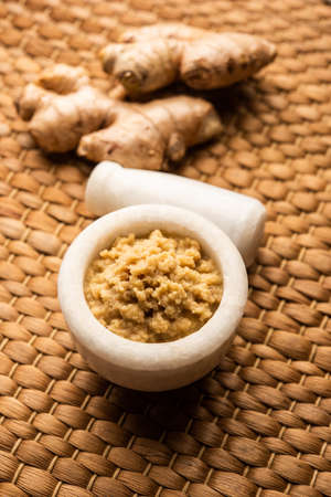Fresh mashed ginger paste or Puree in a bowl and whole Adrak over moody background, selective focusの写真素材