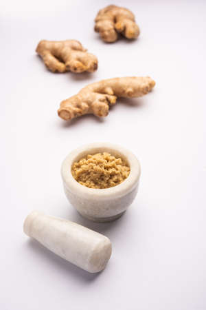 Fresh mashed ginger paste or Puree in a bowl and whole Adrak over moody background, selective focus