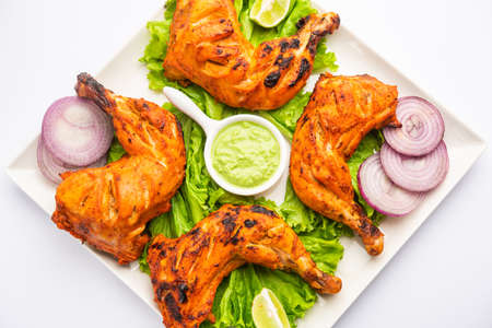 Tandoori chicken is a chicken dish prepared by roasting chicken marinated in yogurt and spices in a tandoor or a clay oven, served with onion and green chutneyの写真素材