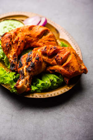 Tandoori chicken is a chicken dish prepared by roasting chicken marinated in yogurt and spices in a tandoor or a clay oven, served with onion and green chutneyの写真素材